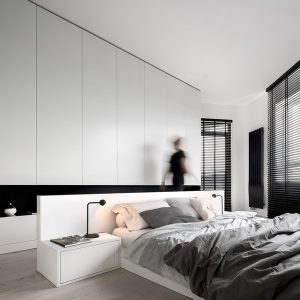 Woman walking in luxury bedroom interior in black and white, with big bed and big wardrobe